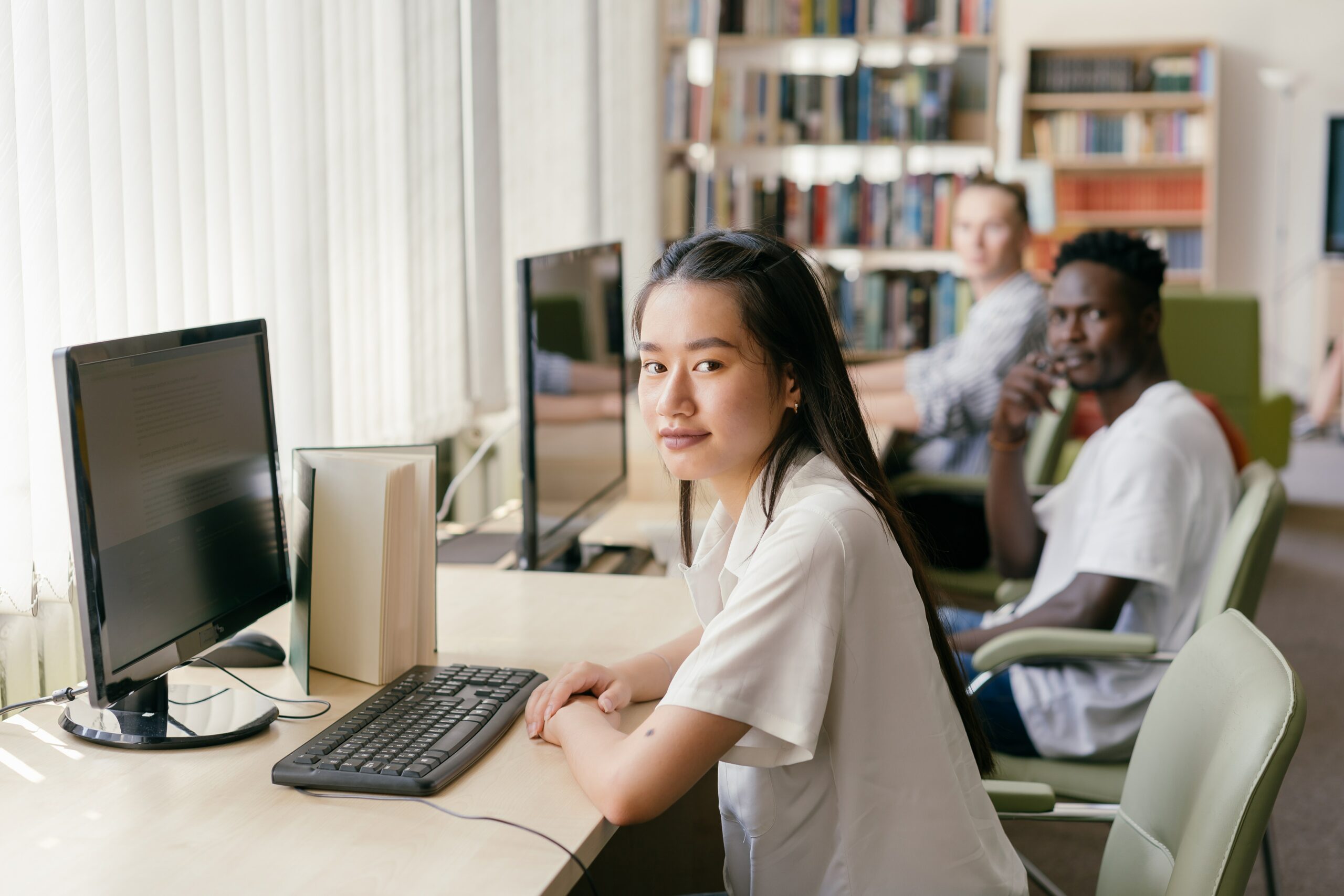 Three students sitting in front of computers in a library.