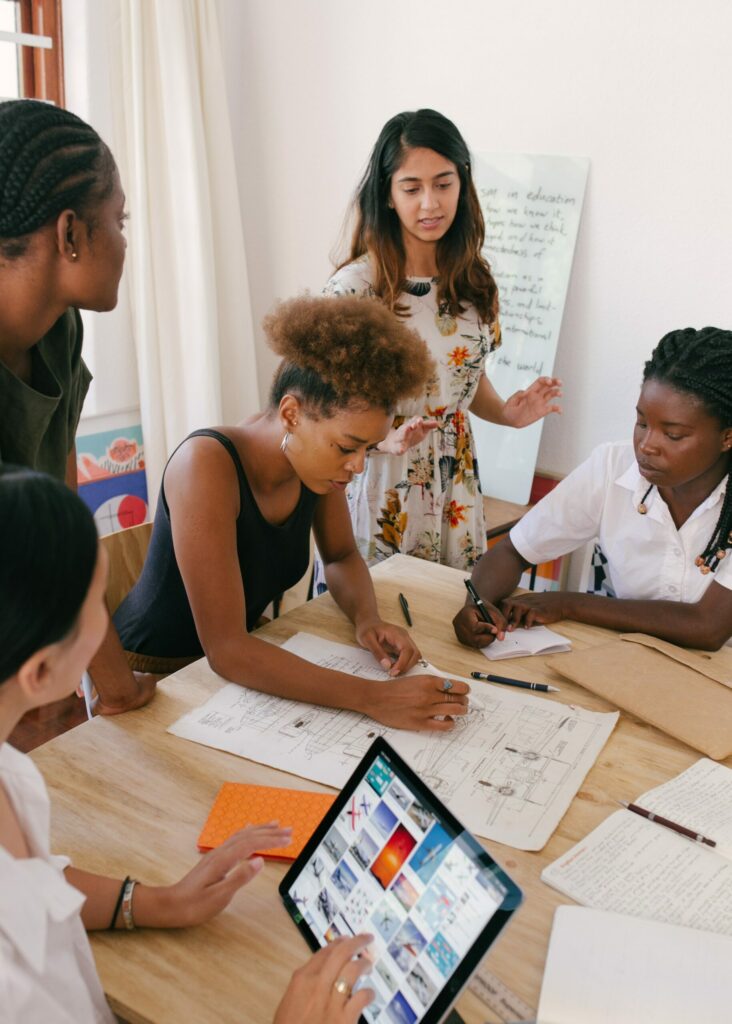 Group of students working around a table using a laptop and writing on paper.